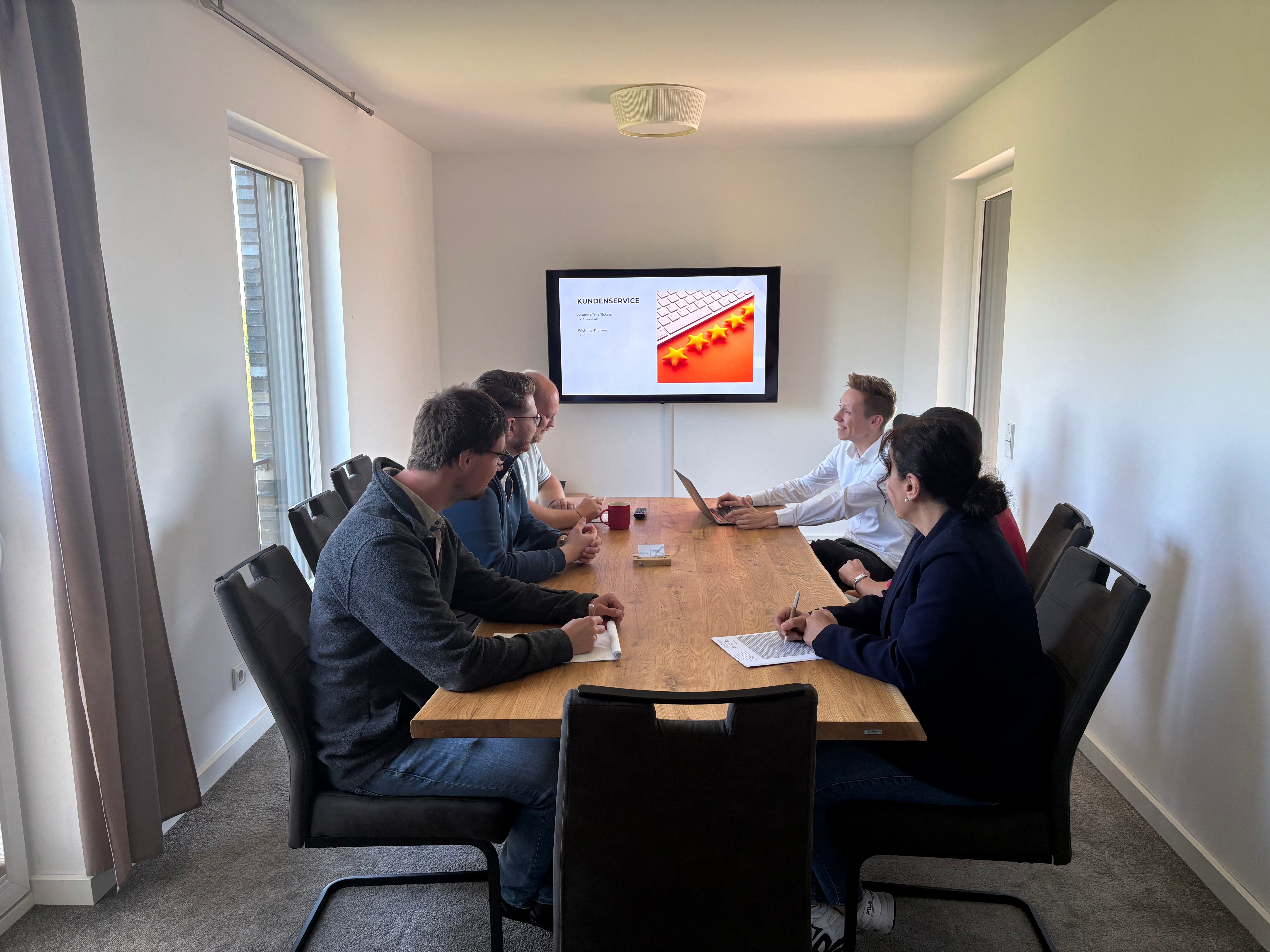 Team van holz4home tijdens een bespreking aan een eikenhouten tafel met presentatie op het scherm