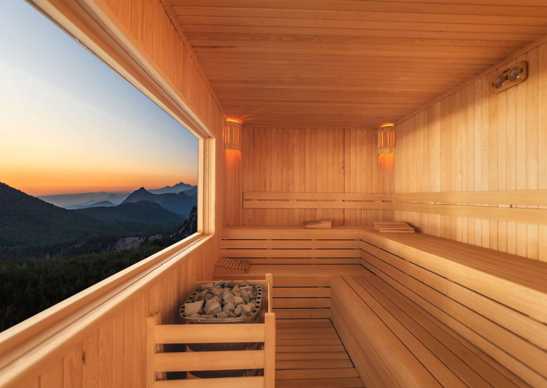 Interieur van een houten barrelsauna met panoramaraam en uitzicht op bergen bij zonsondergang
