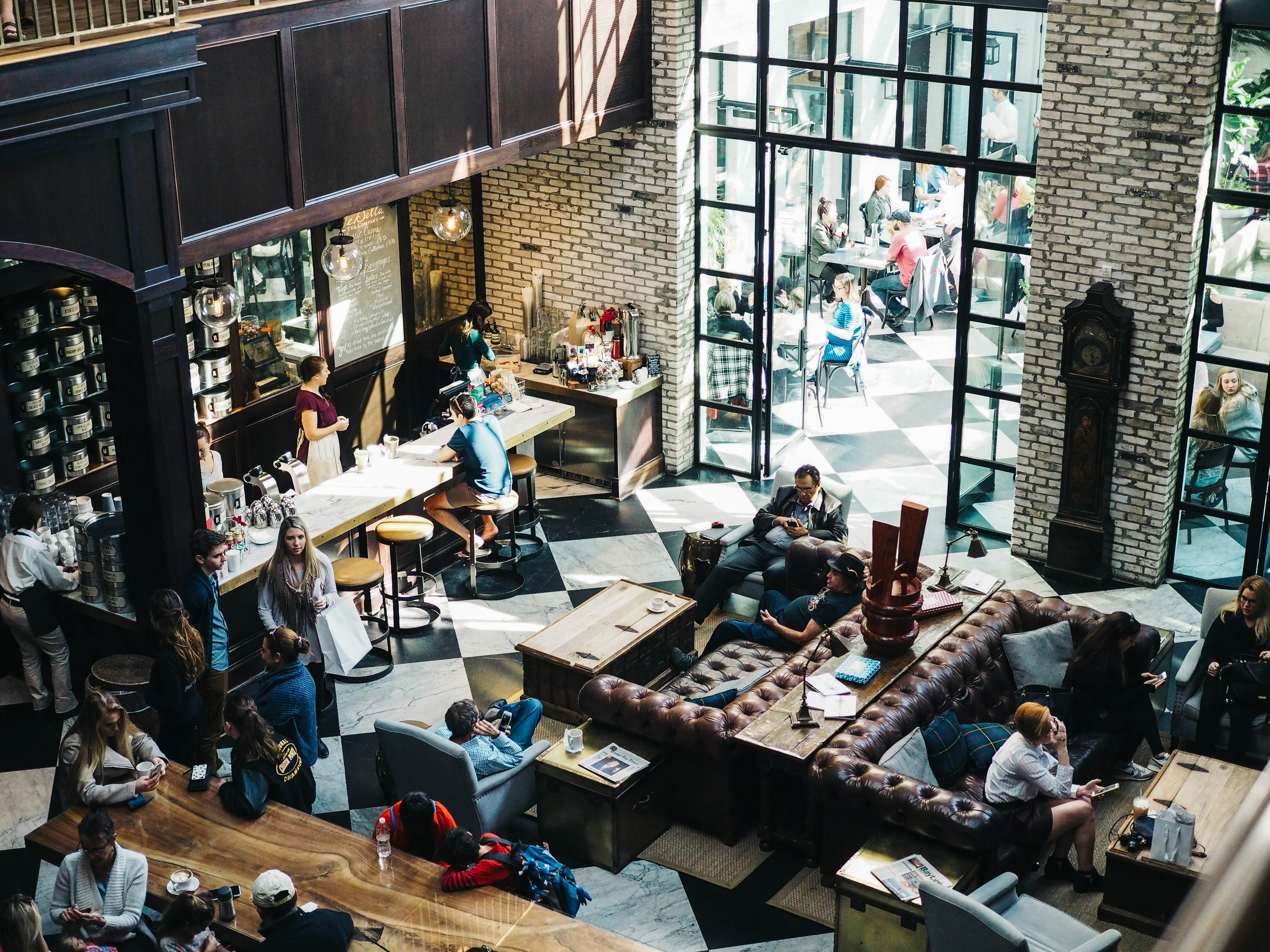 Levendig café in industriële stijl met leren banken, bakstenen muren en grote vensters met roedeverdeling
