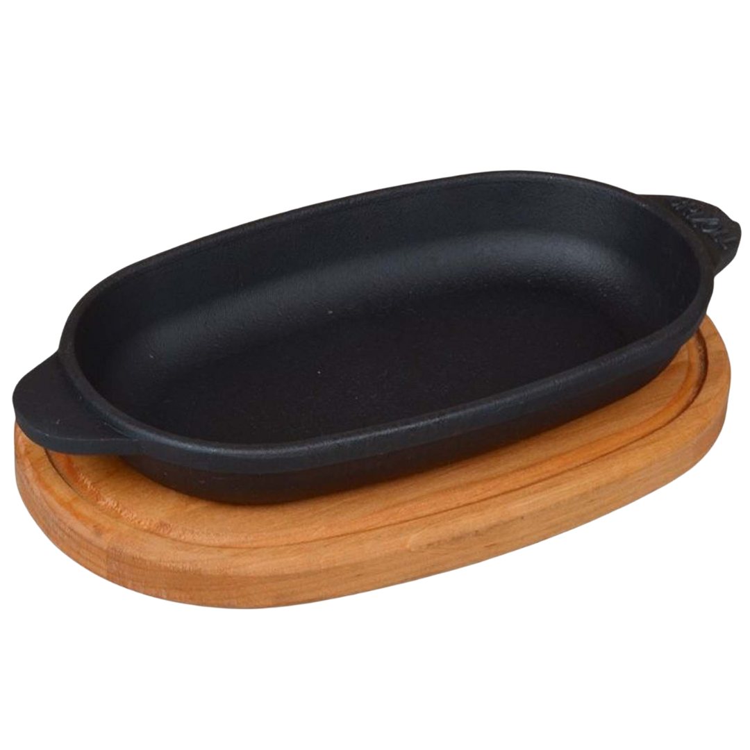 Ovale serveerpan van gietijzer met twee handvatten op een ovale houten onderzetter