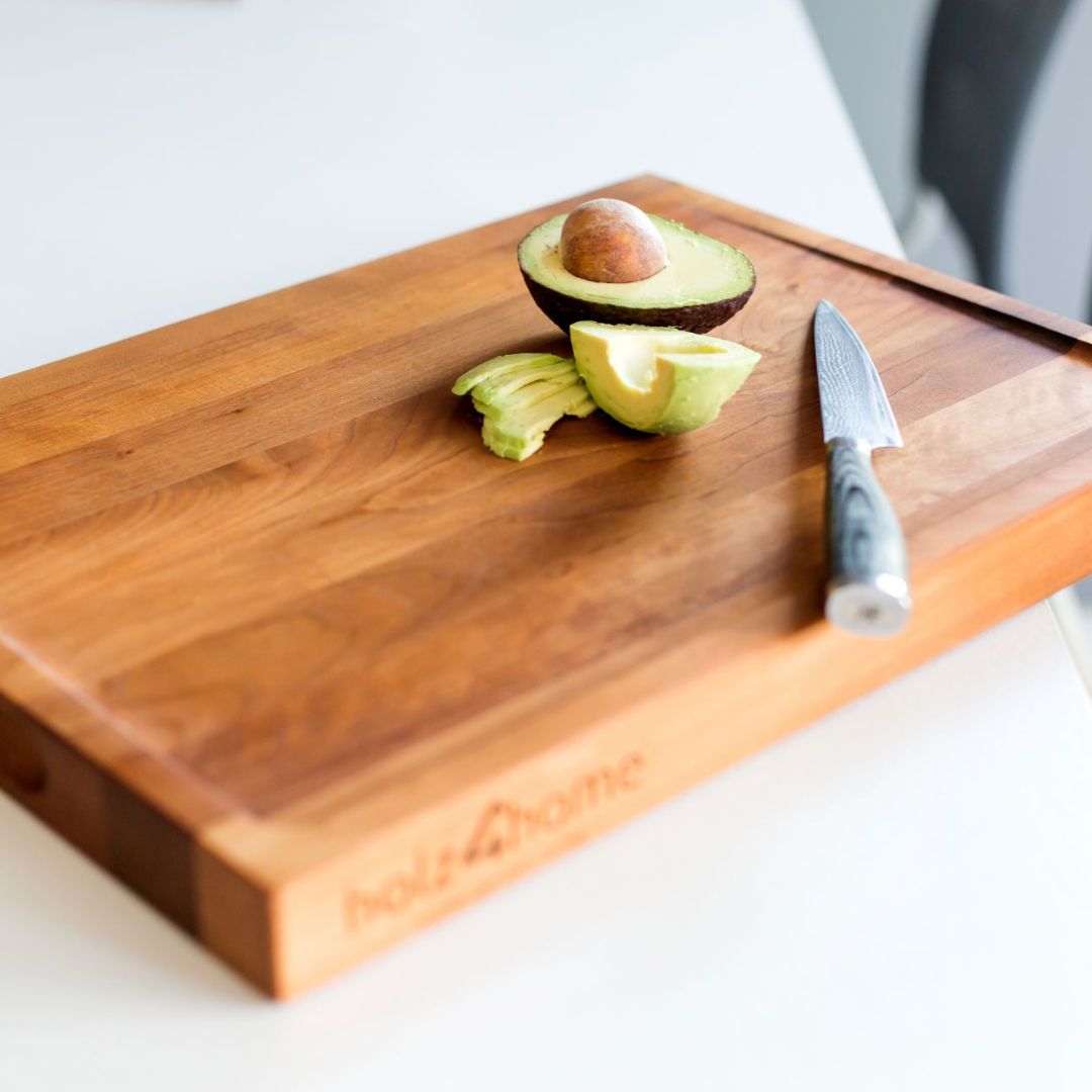 Snijplank van berkenhout met opengesneden avocado en een mes op een wit keukenblad