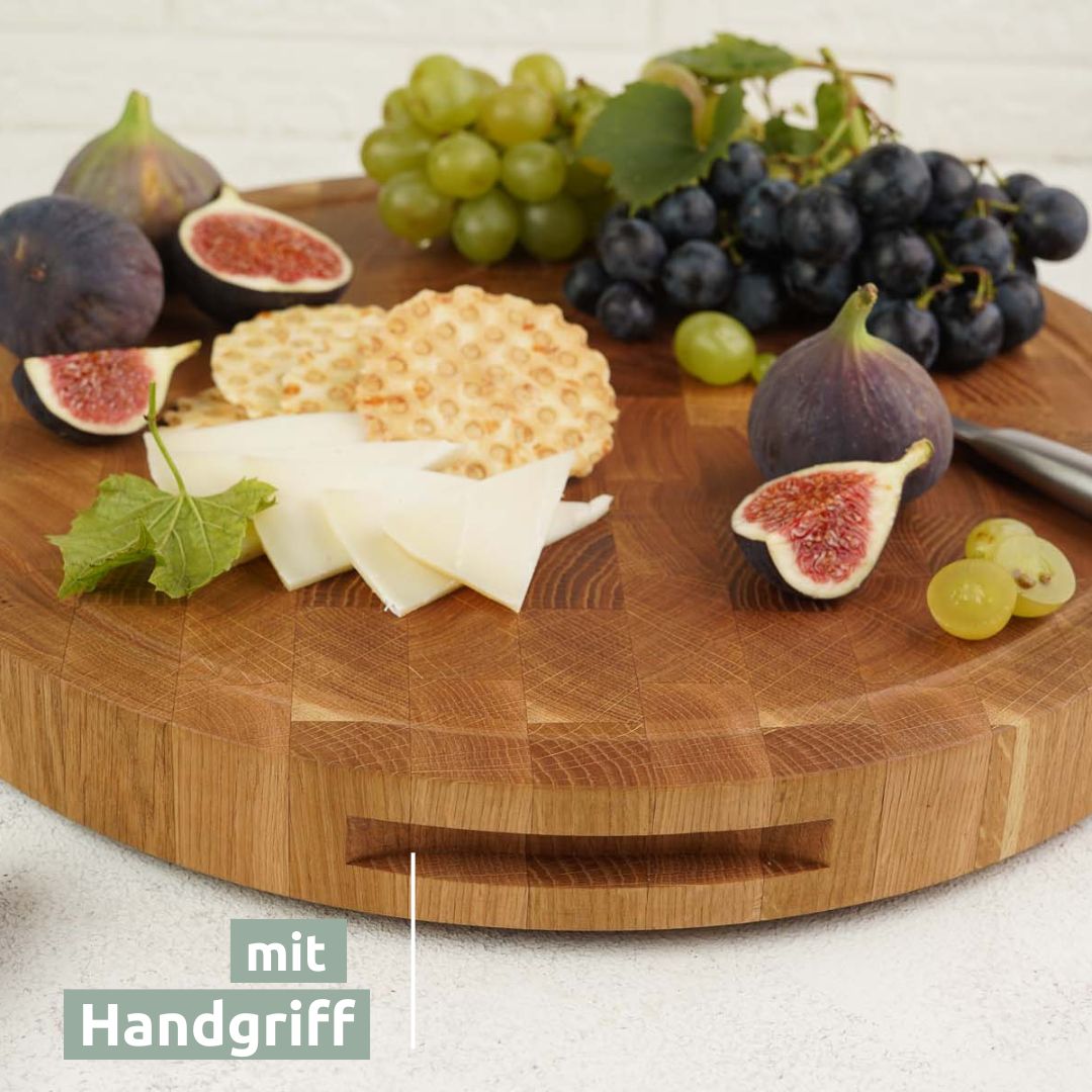 Ronde eikenhouten snijplank met handgreep aan de zijkant, aangericht met kaas en fruit