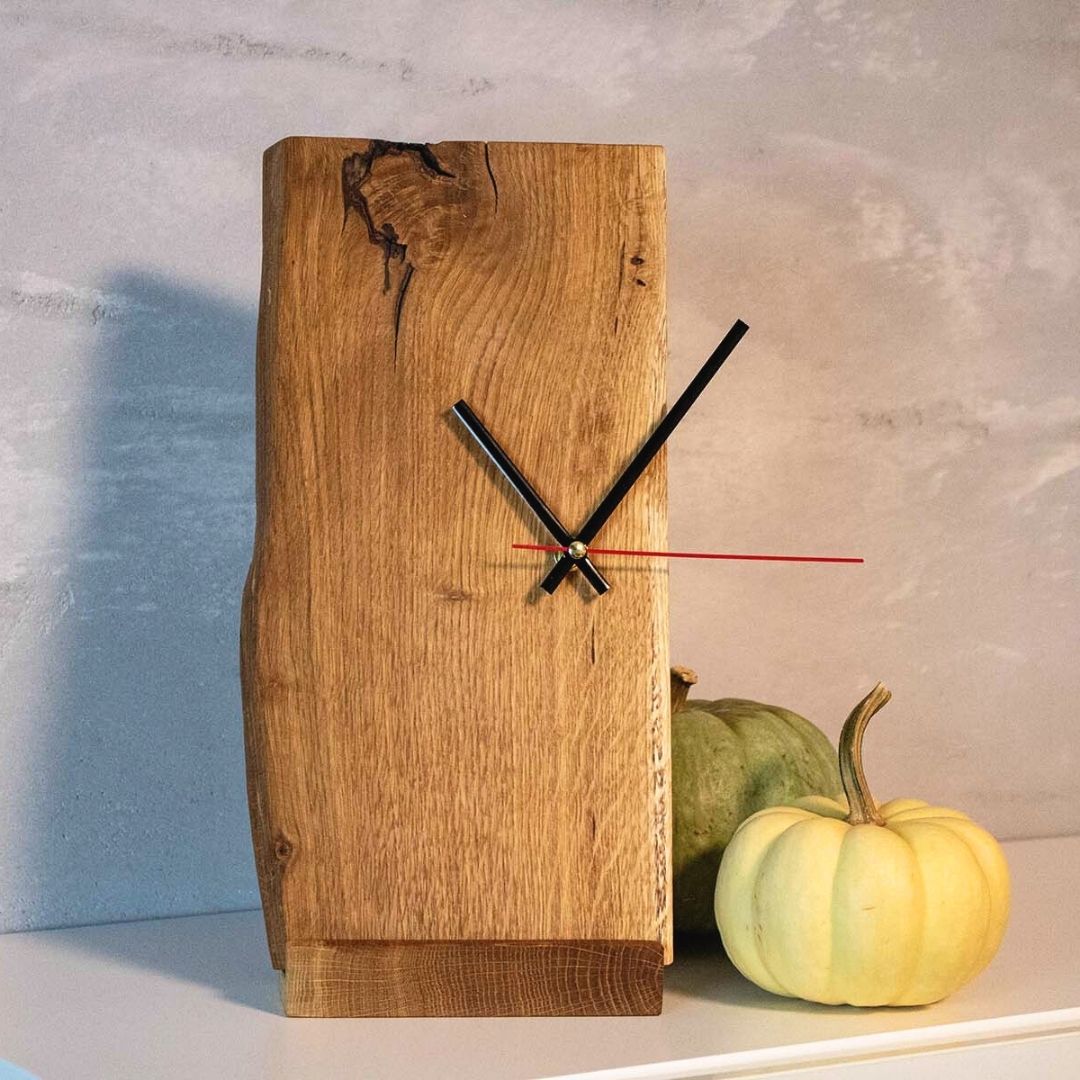 Staande klok van eikenhout met boomstamrand op een plank naast twee decoratieve pompoenen voor een grijze muur
