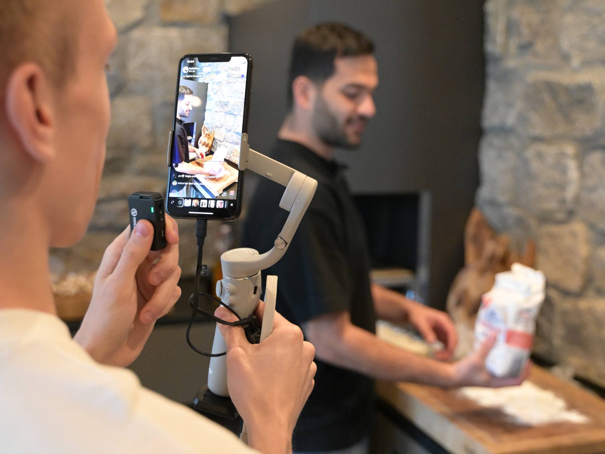 Twee mannen produceren content met smartphone en gimbal voor een stenen muur bij de open haard