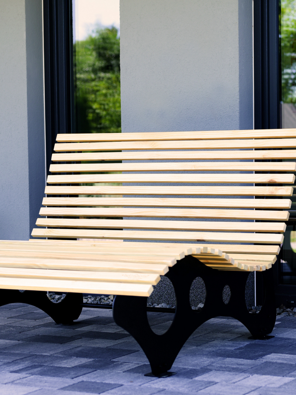 Houten ligstoel van grenenhout met gebogen lattenoppervlak op een bestraat terras bij het huis