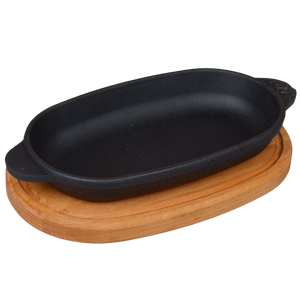 Ovale serveerpan van gietijzer met twee handvatten op een ovale houten onderzetter