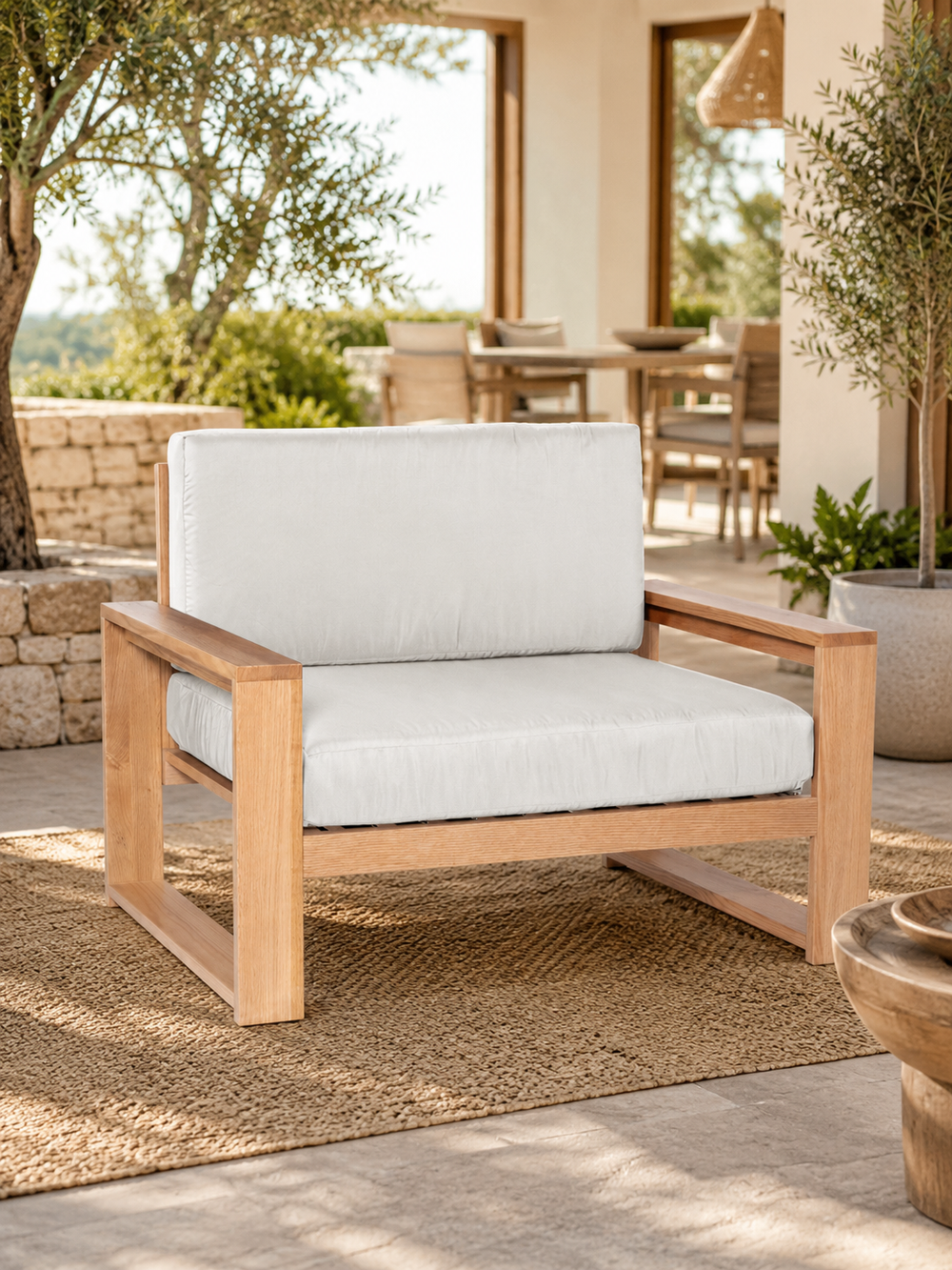 Tuinlounge-fauteuil van eiken met crèmewitte kussens op een mediterraan terras met zeezicht