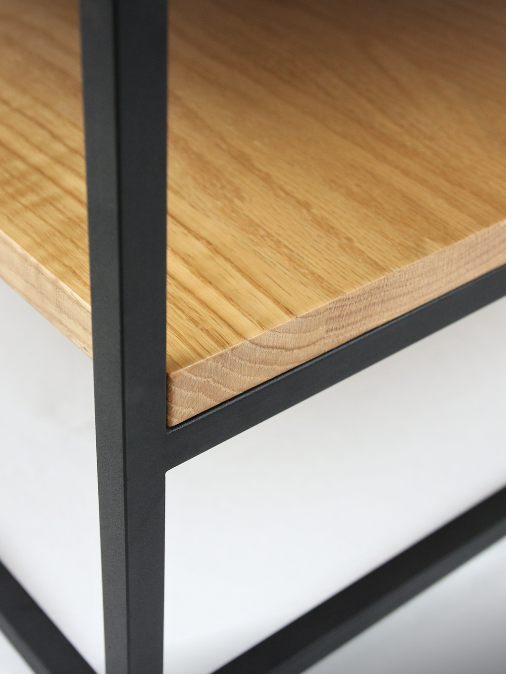 Hoekdetail van de kleinere salontafel met onderste legplank van eiken en zwart metalen frame