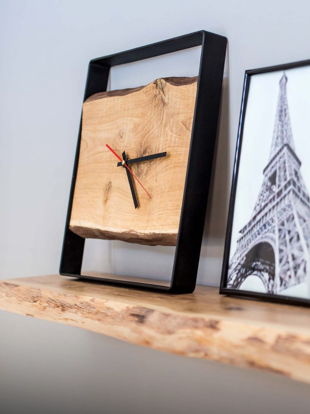 Wandklok met stalen frame en eikenplank op een eiken rek naast een ingelijste Eiffeltoren-afbeelding