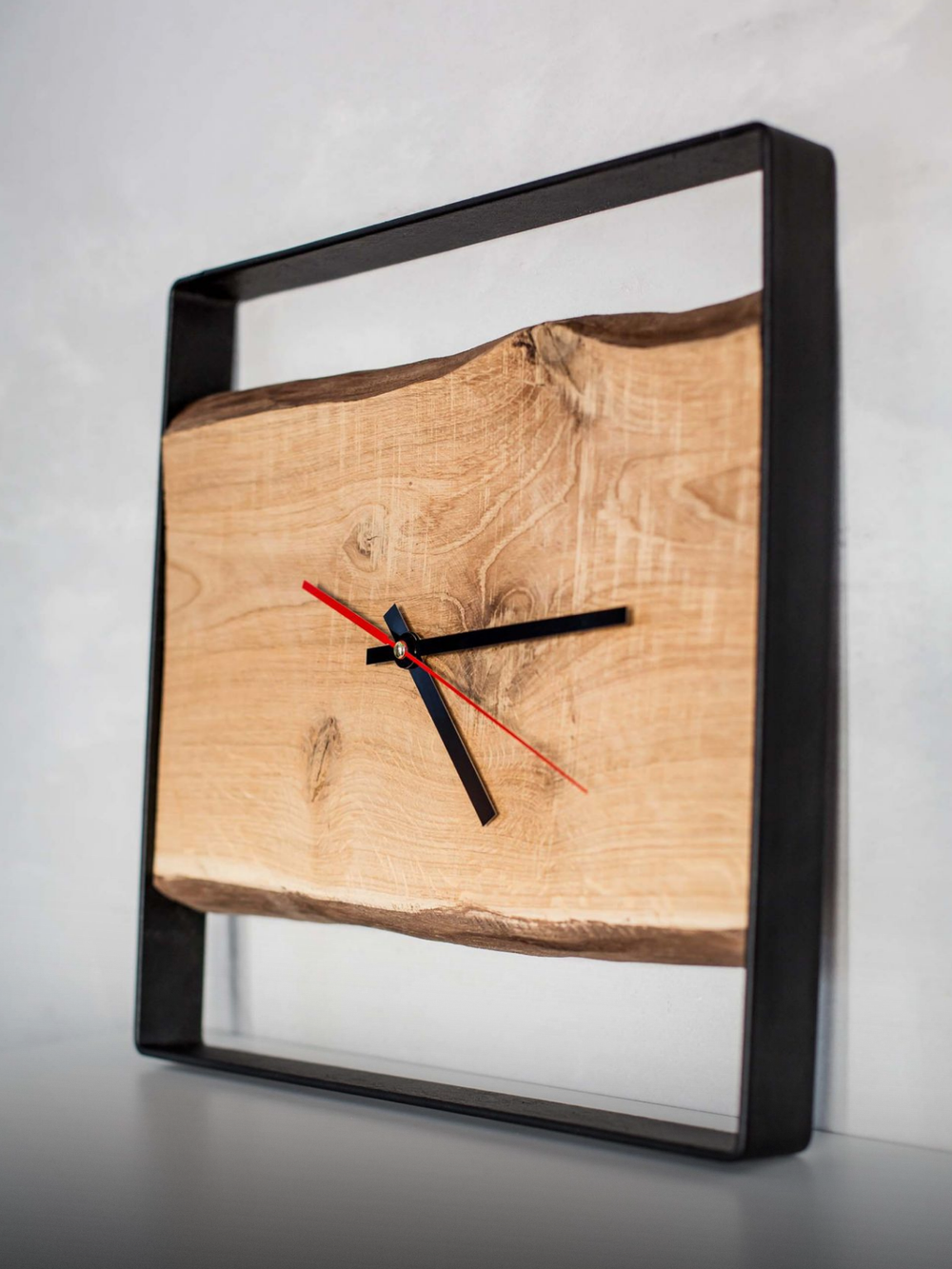 Vierkante wandklok met zwart stalen frame en eikenplank, zijaanzicht tegen een grijze muur