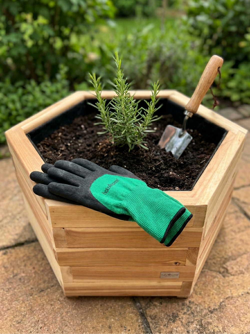 Zeshoekige plantenkuip van grenen met rozemarijn, groene tuinhandschoen en plantschepje in de tuin