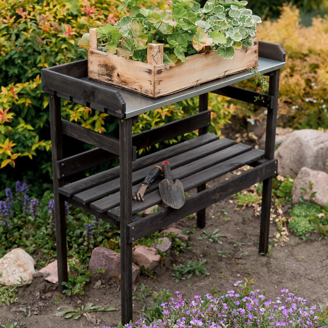Zwarte houten plantentafel van opzij in het plantenbed, onderste legplank met plantenschepje