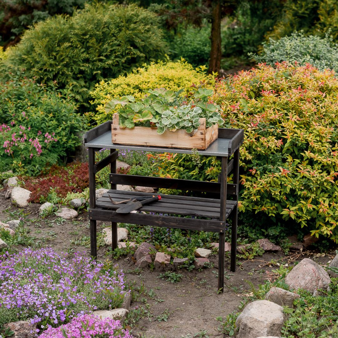 Zwarte houten plantentafel in de tuin tussen bloeiende struiken, beplante houten kist op het werkblad