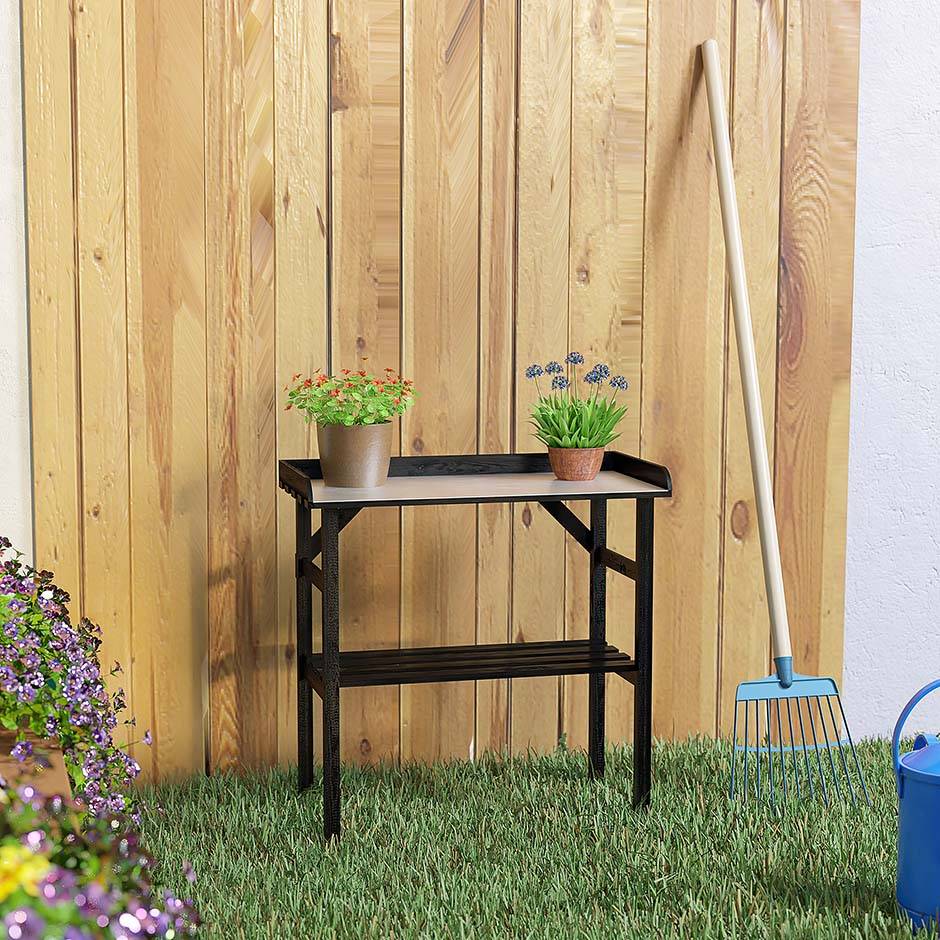 Zwarte houten plantentafel bij een houten wand met twee potplanten en hark in de tuin