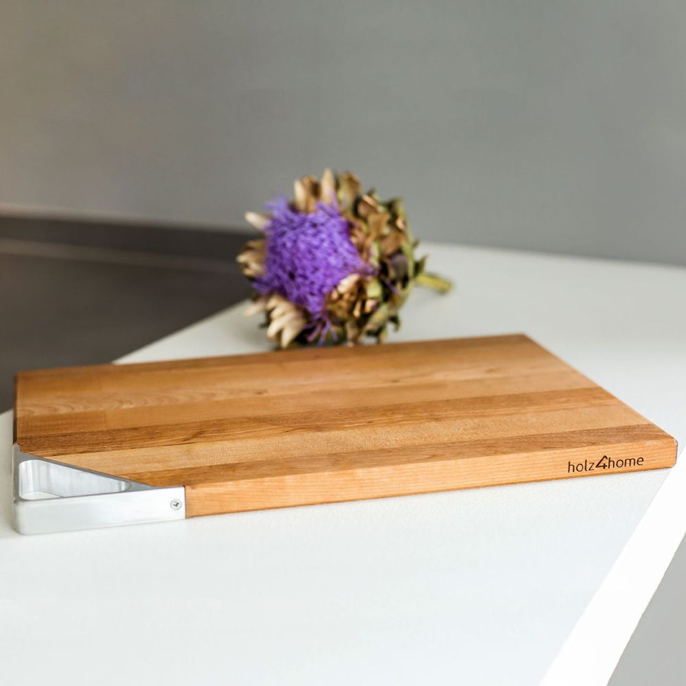 Snijplank van berkenhout met metalen greep op een wit keukenwerkblad met droogbloemen