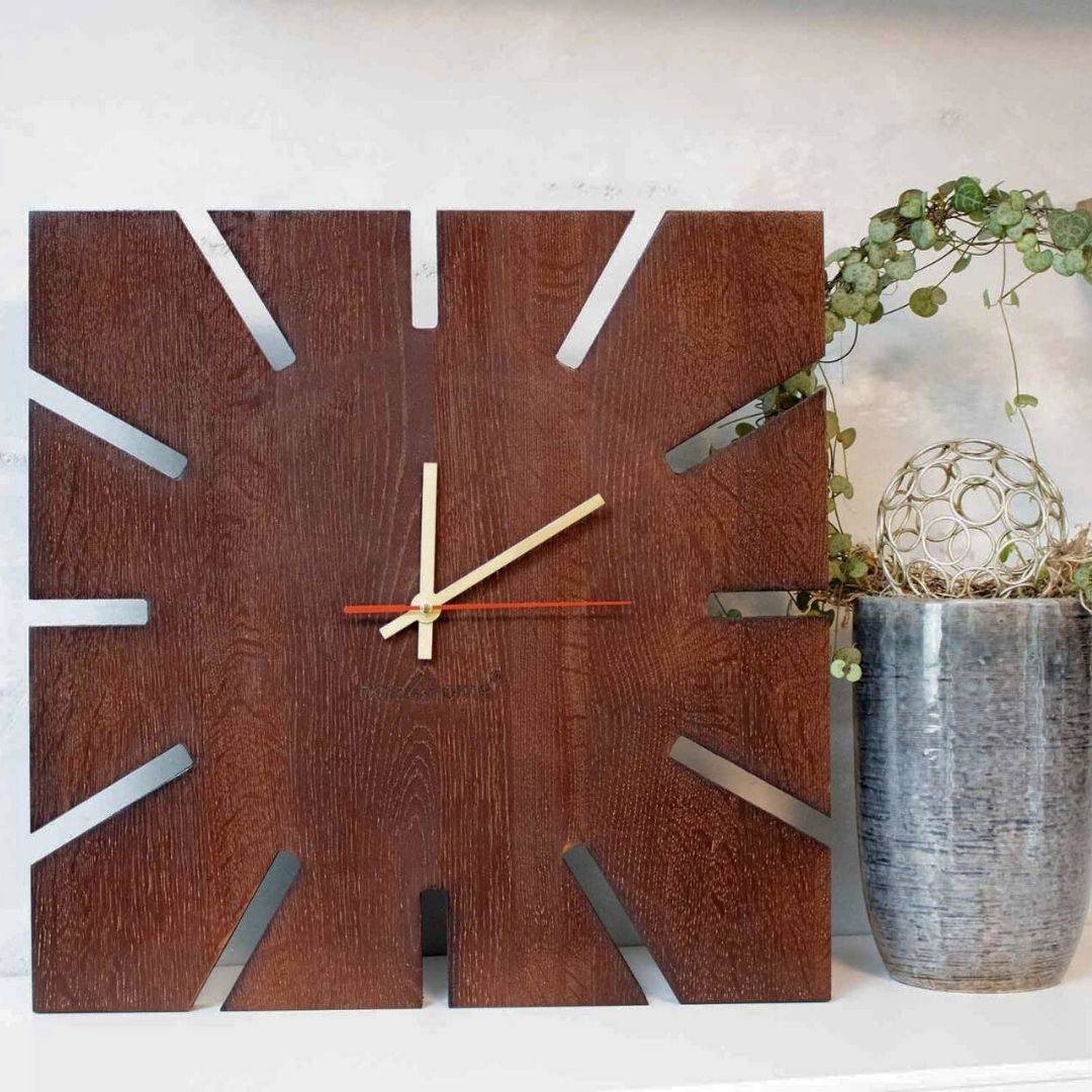 Wandklok Sunshine XL van donker eikenhout met stralendesign naast een grijze vaas met klimplant
