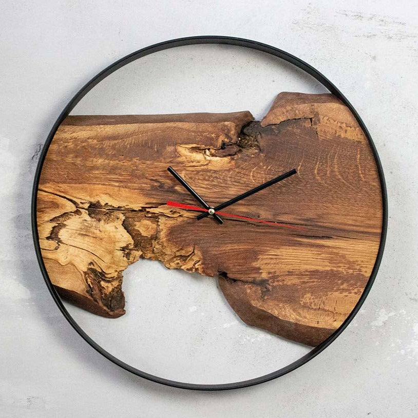 Wandklok Artwork met eikenhouten plank en zwarte ring aan een lichte betonnen muur, met zwarte wijzers
