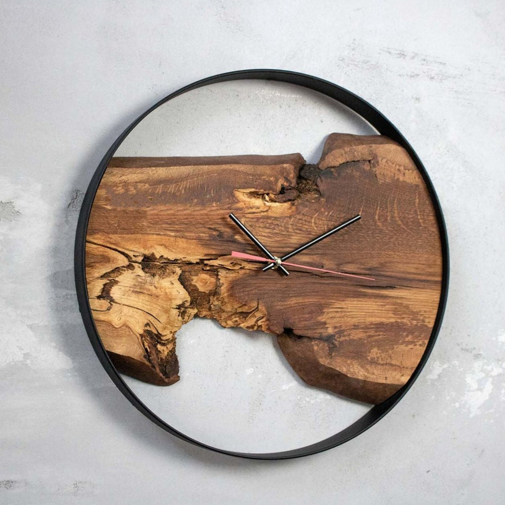 Ronde wandklok Artwork met eikenhouten plank en rode secondewijzer, schuin tegen een grijze betonnen muur