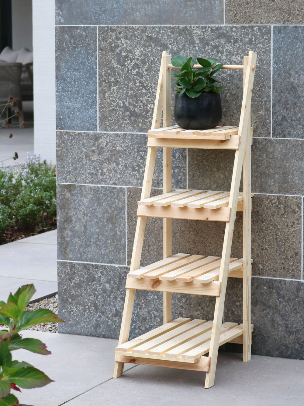 Plantenladder frontaal tegen stenen muur op terras met een groene plant