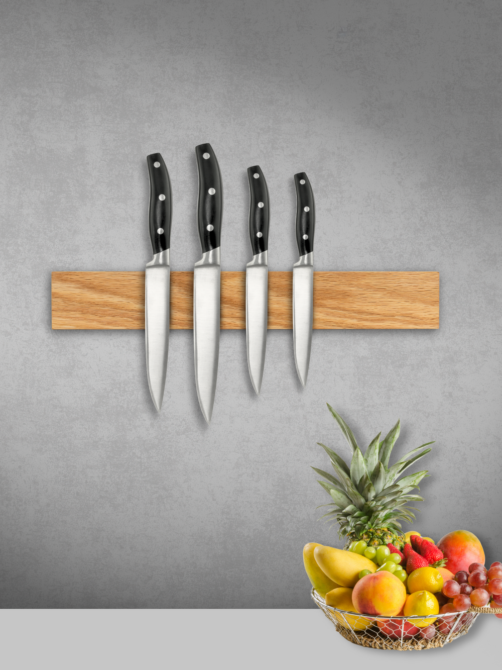Magnetische messenstrip van eiken met vier messen aan een grijze muur boven een fruitmand