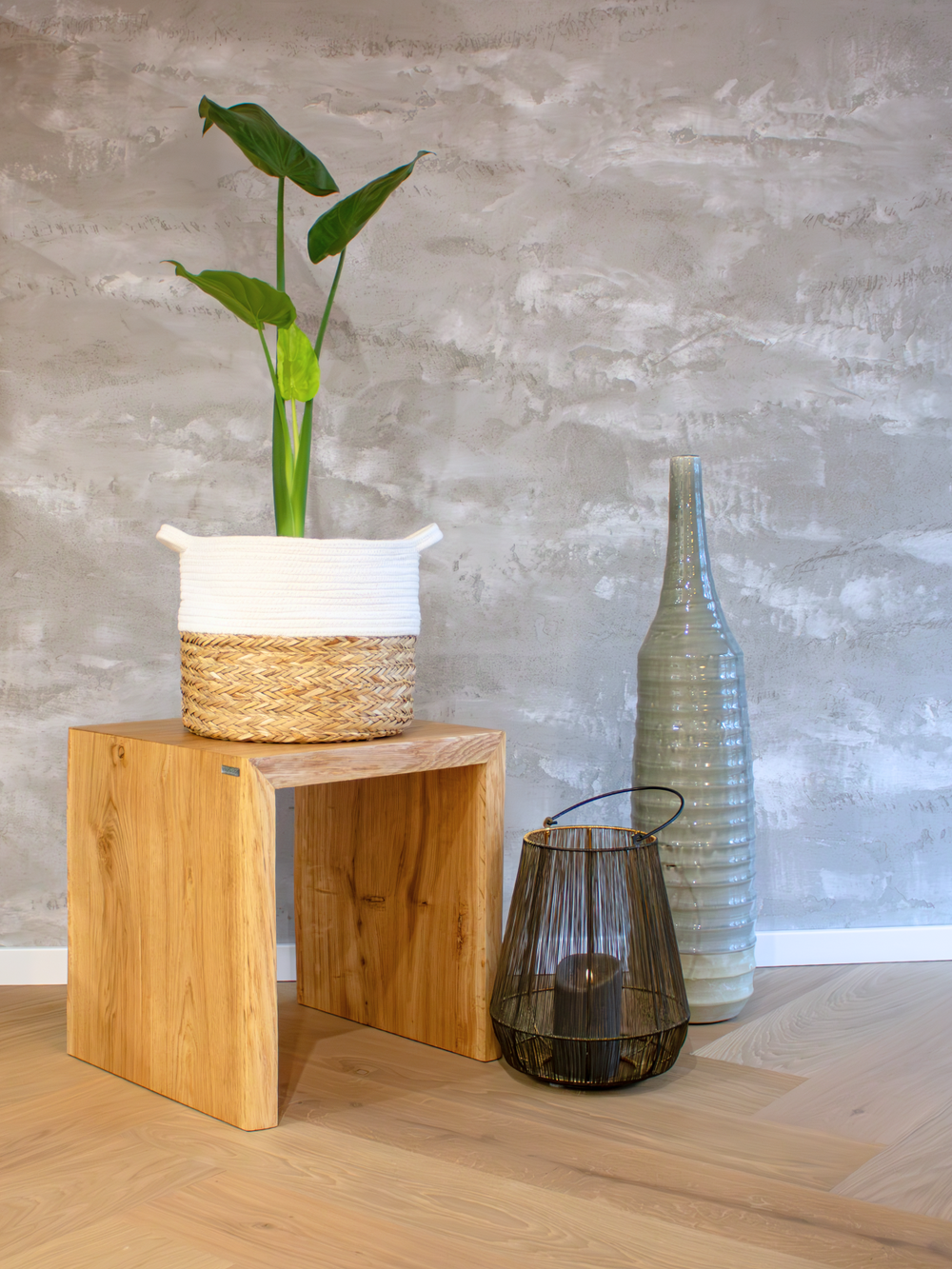 Massief houten kruk van eiken als bijzettafel met plantenmand en lantaarn voor een betonnen muur