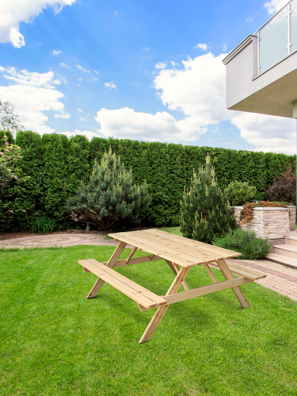 Picknicktafel van vurenhout in de tuin op het gazon voor een groene haag en terras