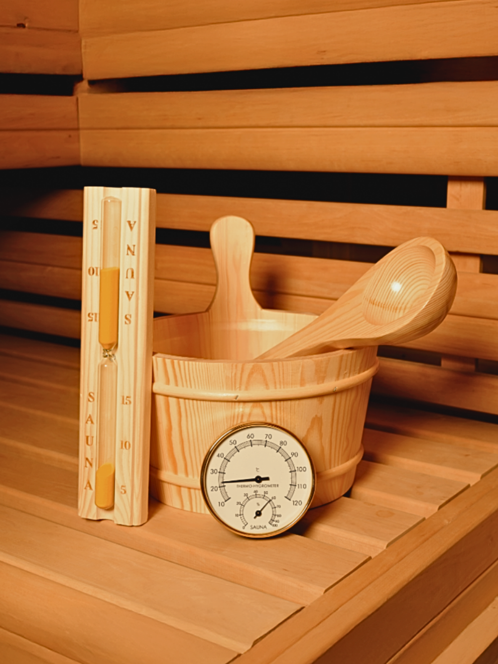 Saunaset van grenenhout met emmer, schepper, zandloper en thermometer op een houten saunabank