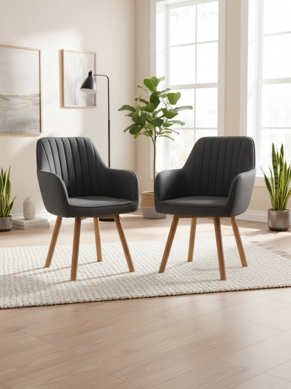 Twee antracietkleurige eetkamerstoelen met eikenpoten in de lichte woonkamer met kamerplant en vloerlamp