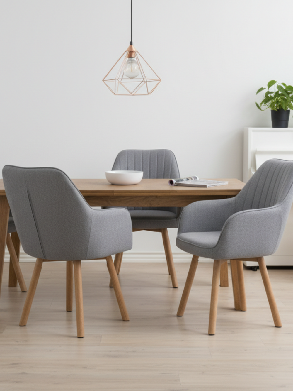 Grijze eetkamerstoelen aan een houten tafel met koperen hanglamp en kruidenpot in de lichte eetkamer