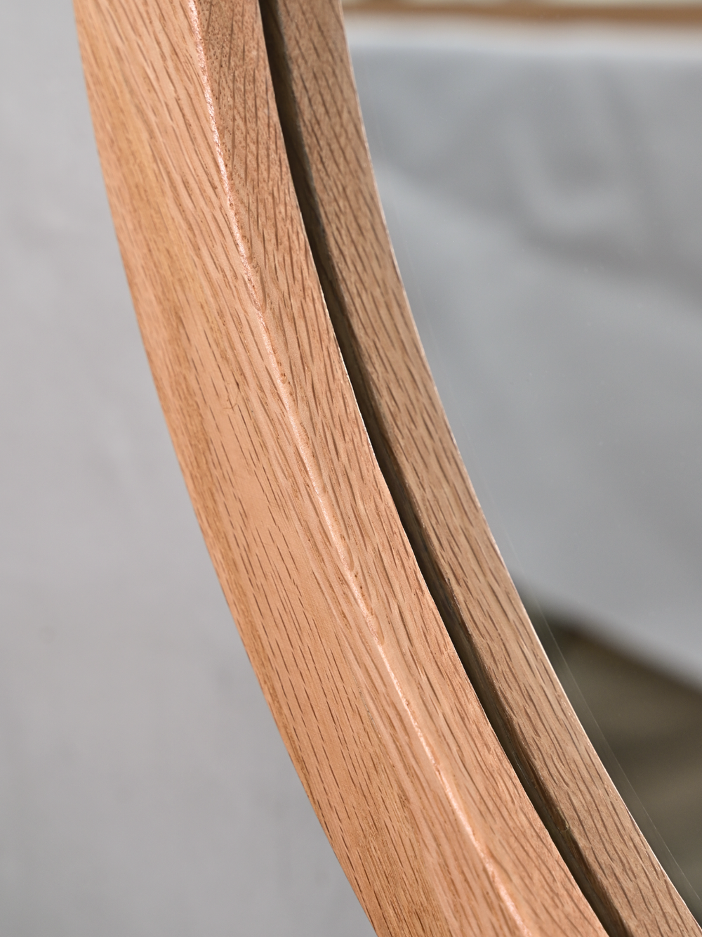 Detailopname van de afgeronde eikenhouten lijst en de spiegelrand bij de ronde wandspiegel, close-up