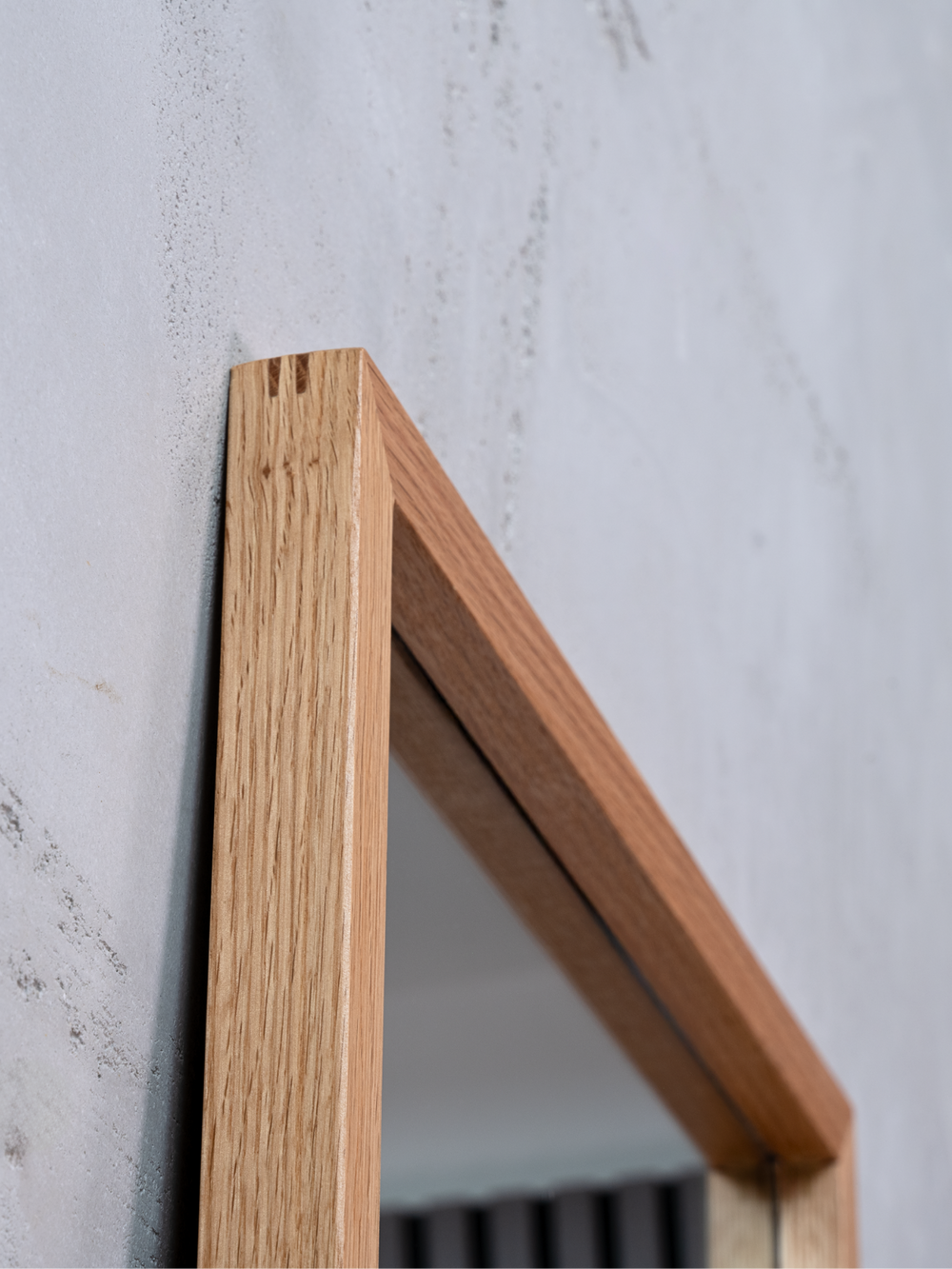 Detailopname van de bovenhoek van de eikenhouten lijst bij de wandspiegel voor een grijze betonwand