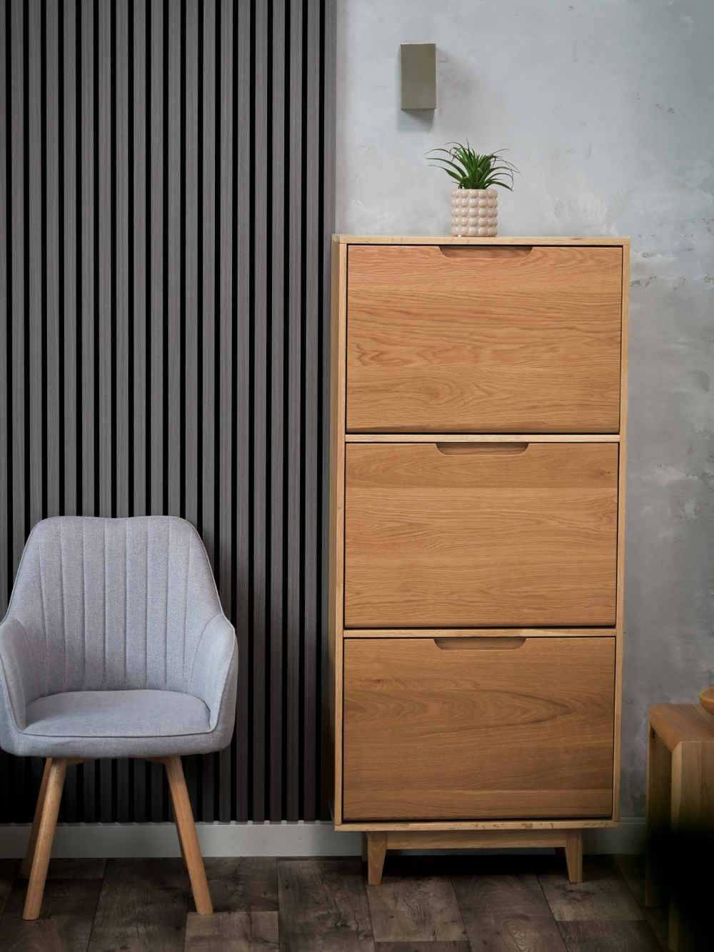 Kiepschoenenkast van eiken naast een grijze fauteuil voor een muur met akoestische panelen en kamerplant