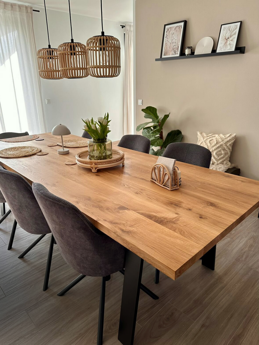 Massief houten tafel eiken met boomstamrand in de gedekte eetkamer, donkere stoelen, rotanlampen en kamerplant