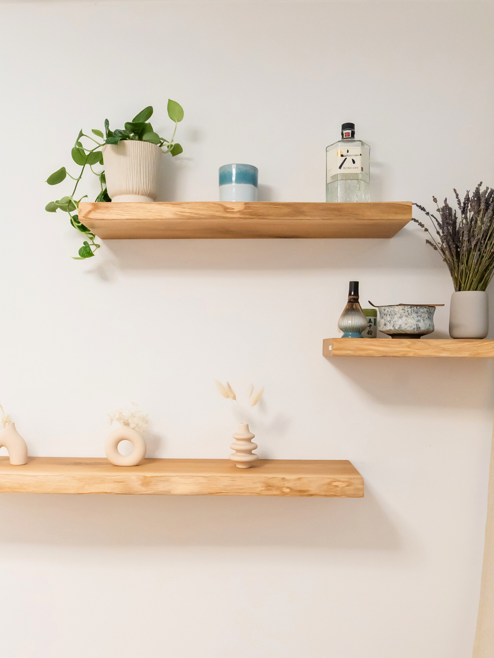 Drie zwevende wandrekken van eiken aan een witte muur, gedecoreerd met planten, vazen en keramiek