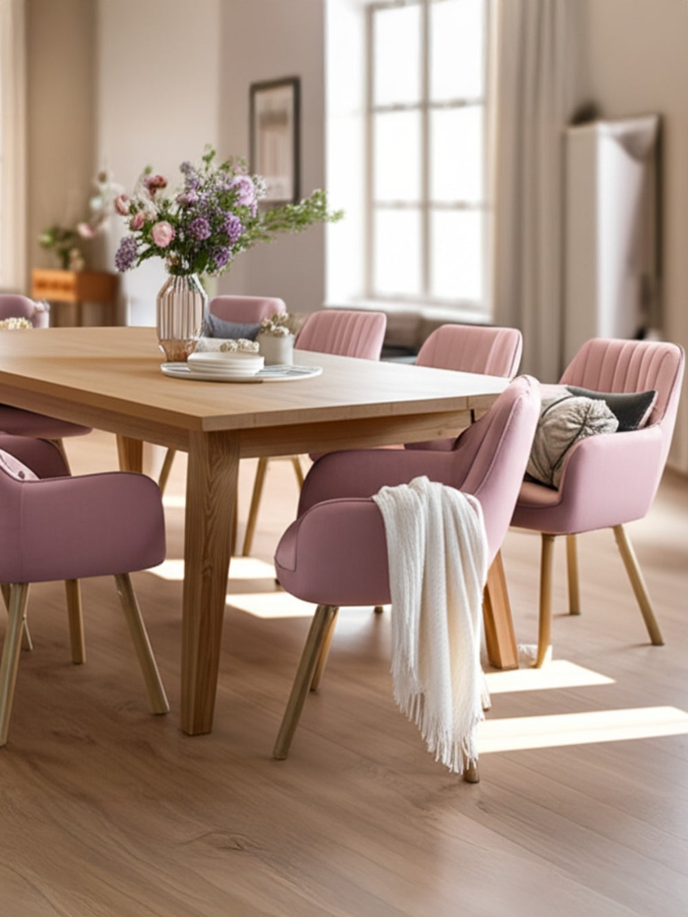 Roze eetkamerstoelen aan een houten tafel met bloemboeket en witte knuffeldeken in de lichte eetkamer