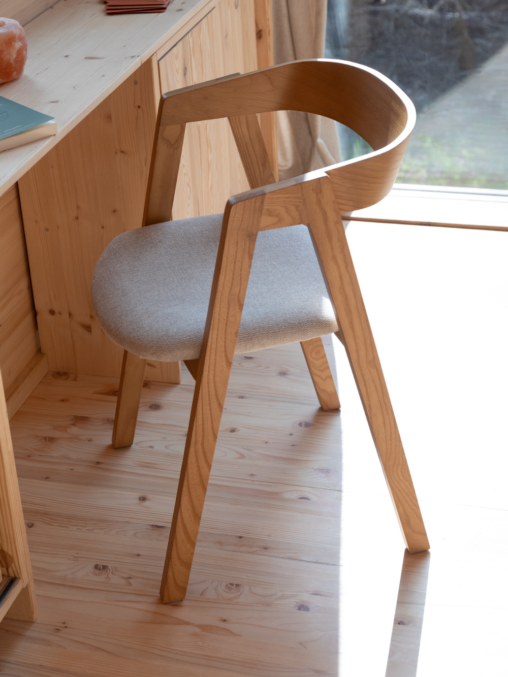 Eetkamerstoel Mads van essen naturel aan een bureau van hout voor het raam in de woonruimte