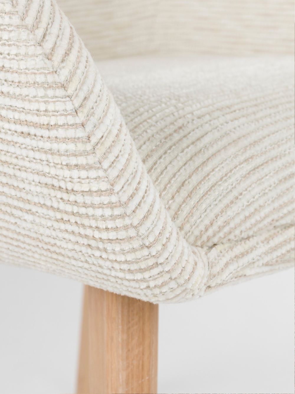 Detailopname van de gebogen armleuning en de geribbelde off-white bekleding bij de armleuningstoel Loua
