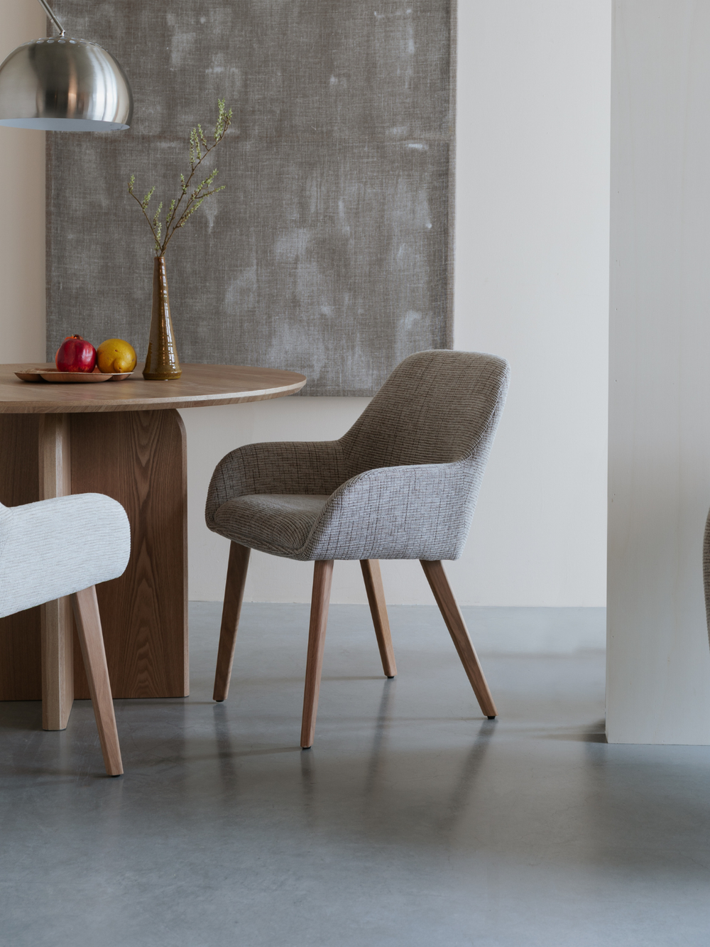 Armleuningstoel Loua aan een ronde eettafel van eiken met droogbloemen en fruitschaal in de eetkamer