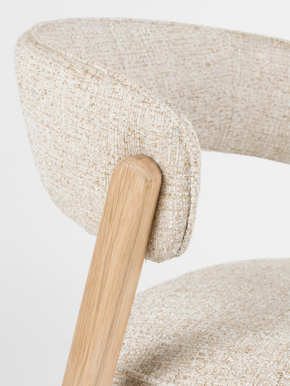 Detailopname van de gebogen rugleuning van bouclé en het eikenhouten onderstel bij de eetkamerstoel Bright