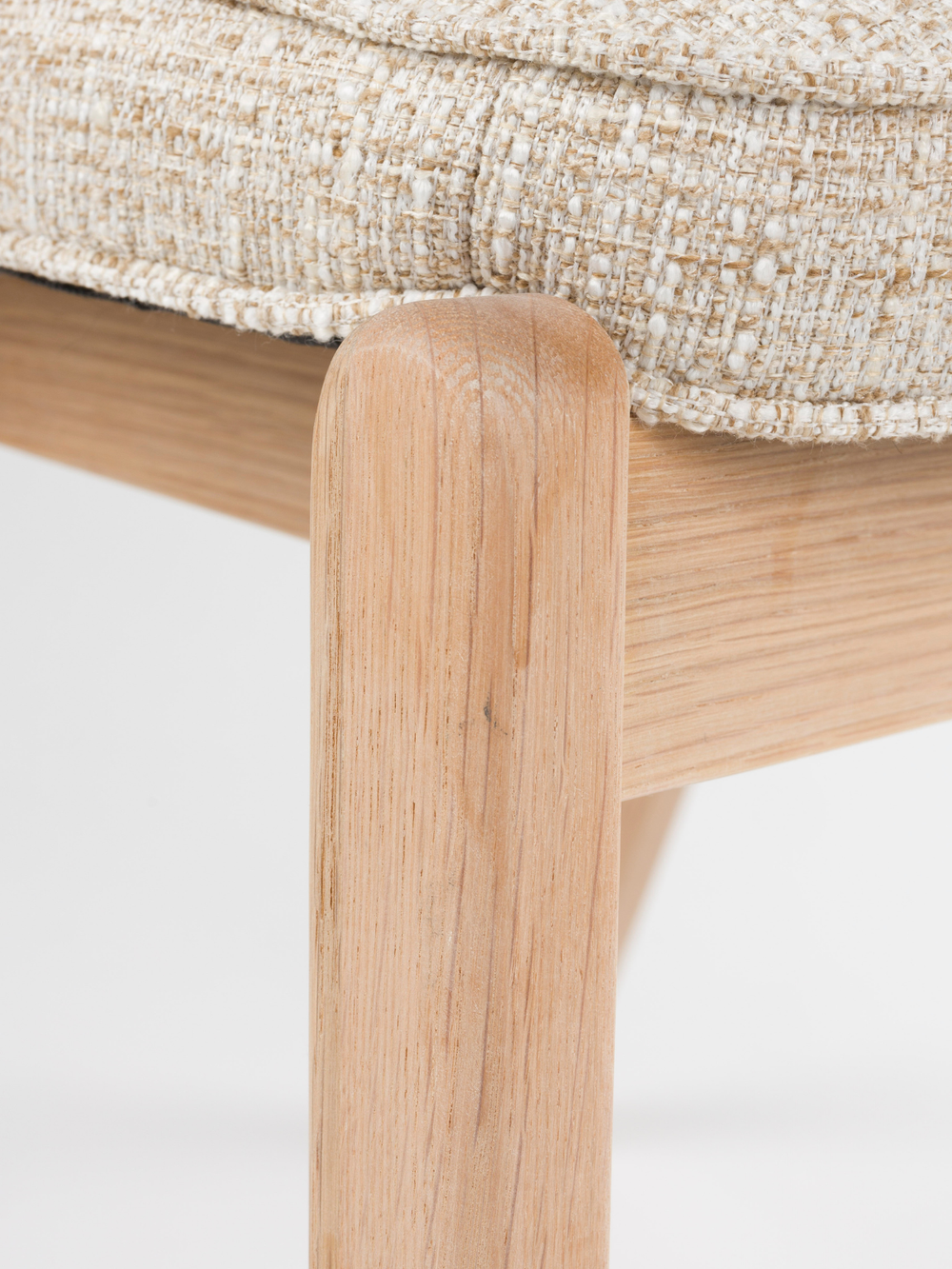 Detailopname van de massief eikenhouten poot en de zitrand bij de eetkamerstoel Bright in beige