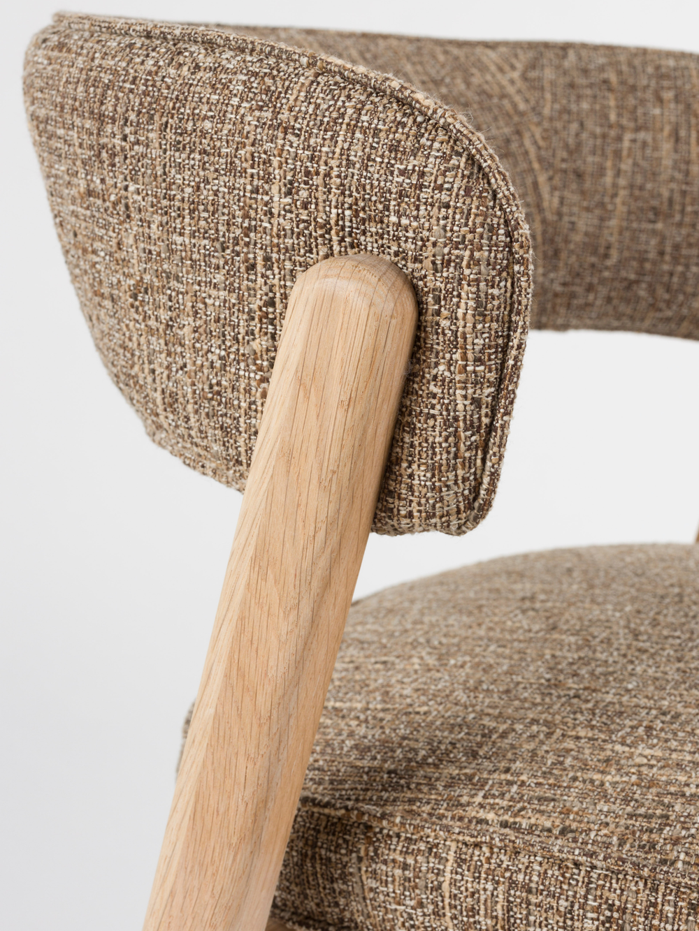 Detailopname van de gebogen rugleuning van bouclé en het eikenhouten onderstel bij de eetkamerstoel Bright