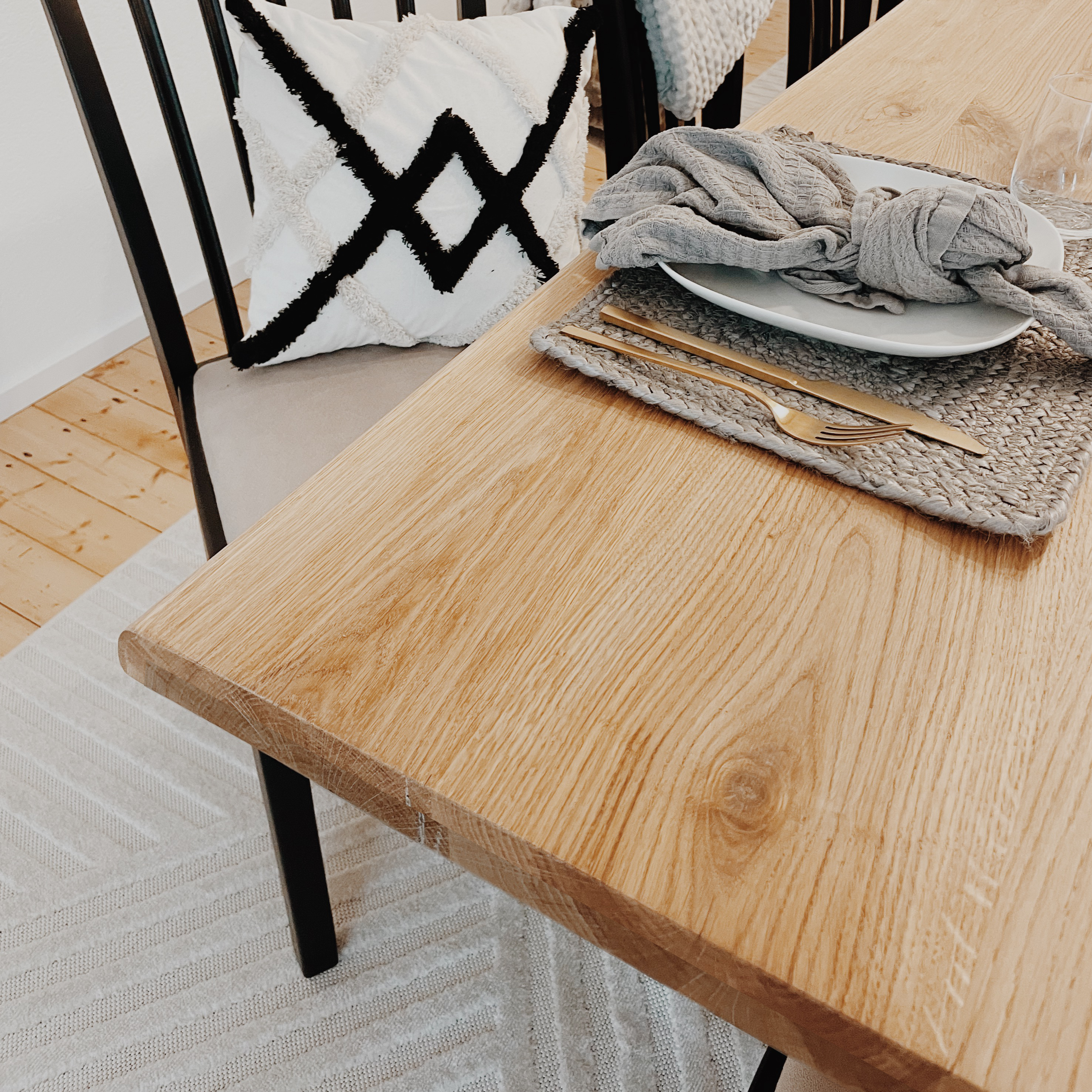 Gedekte tafelhoek van de eikenhouten tafel met boomstamrand, placemat en gouden bestek in de eetkamer
