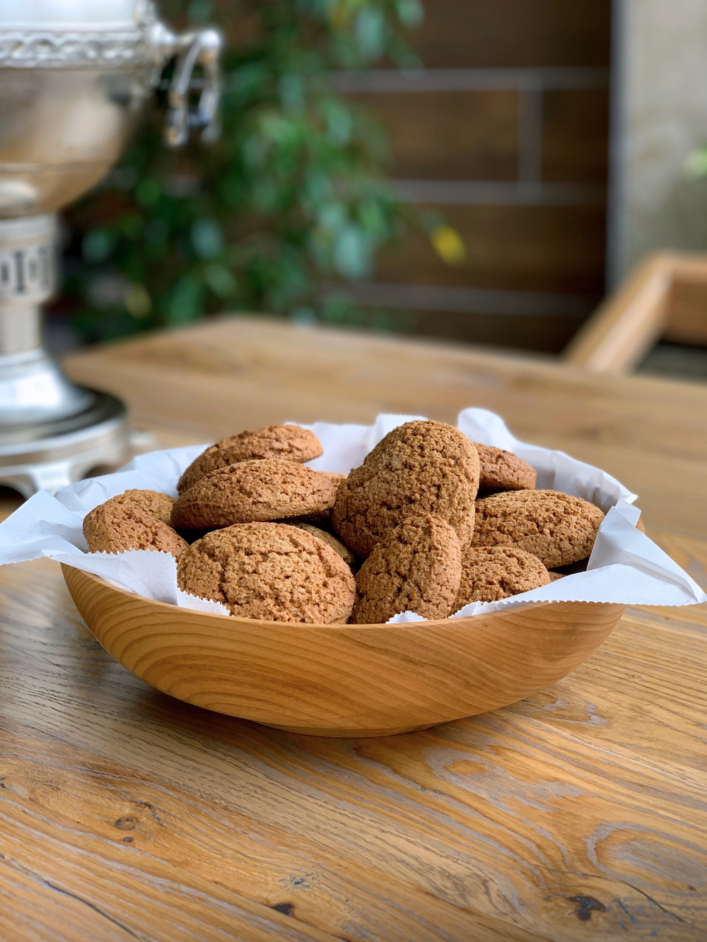 Houten schaal van essenhout gevuld met gebak op een houten tafel naast een zilveren samowar