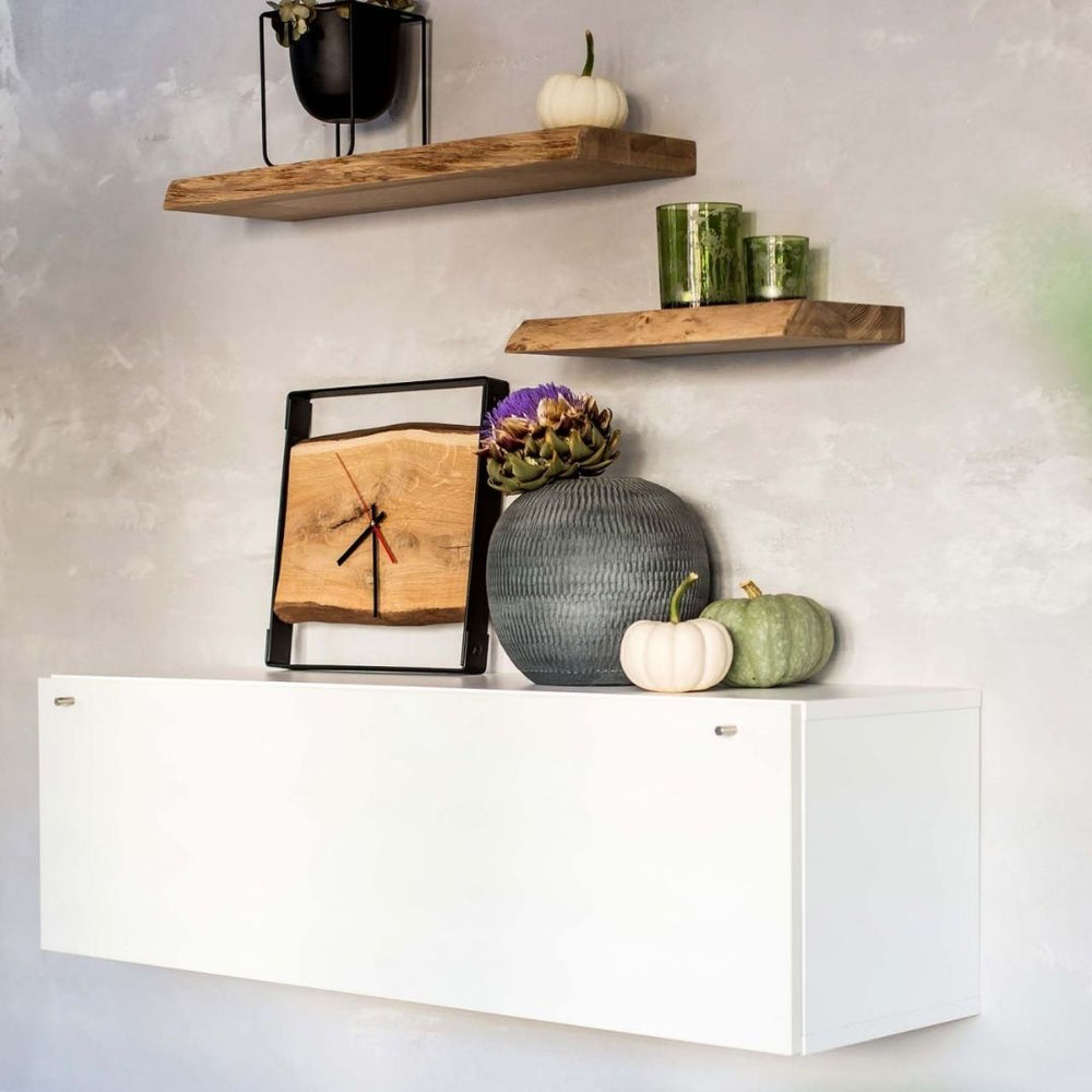 Vierkante wandklok met stalen frame en eikenhouten plank op een dressoir naast zwevende houten wandrekken