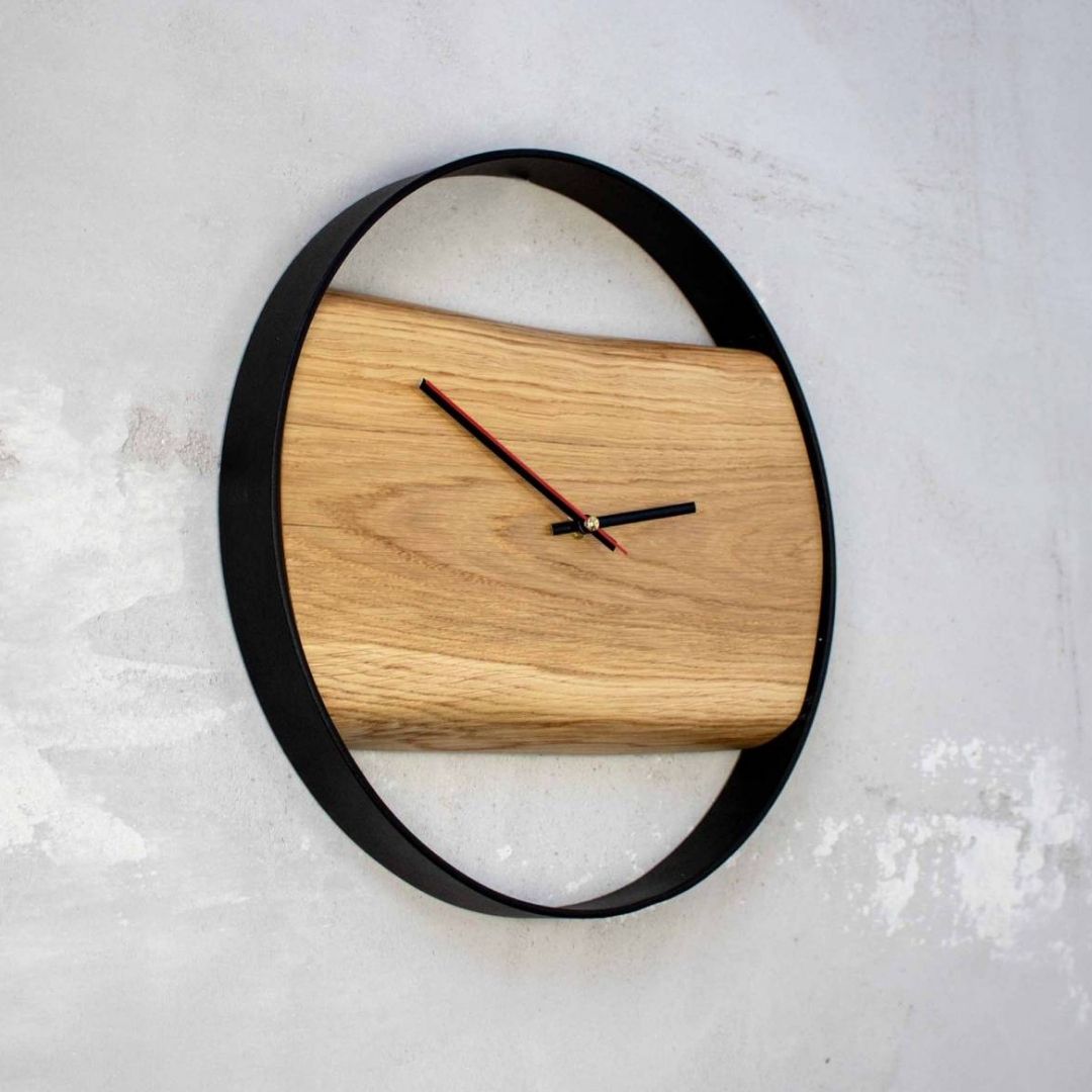 Omlijste houten wandklok Polished van eikenhout aan lichte betonnen muur, licht zijdelings aanzicht
